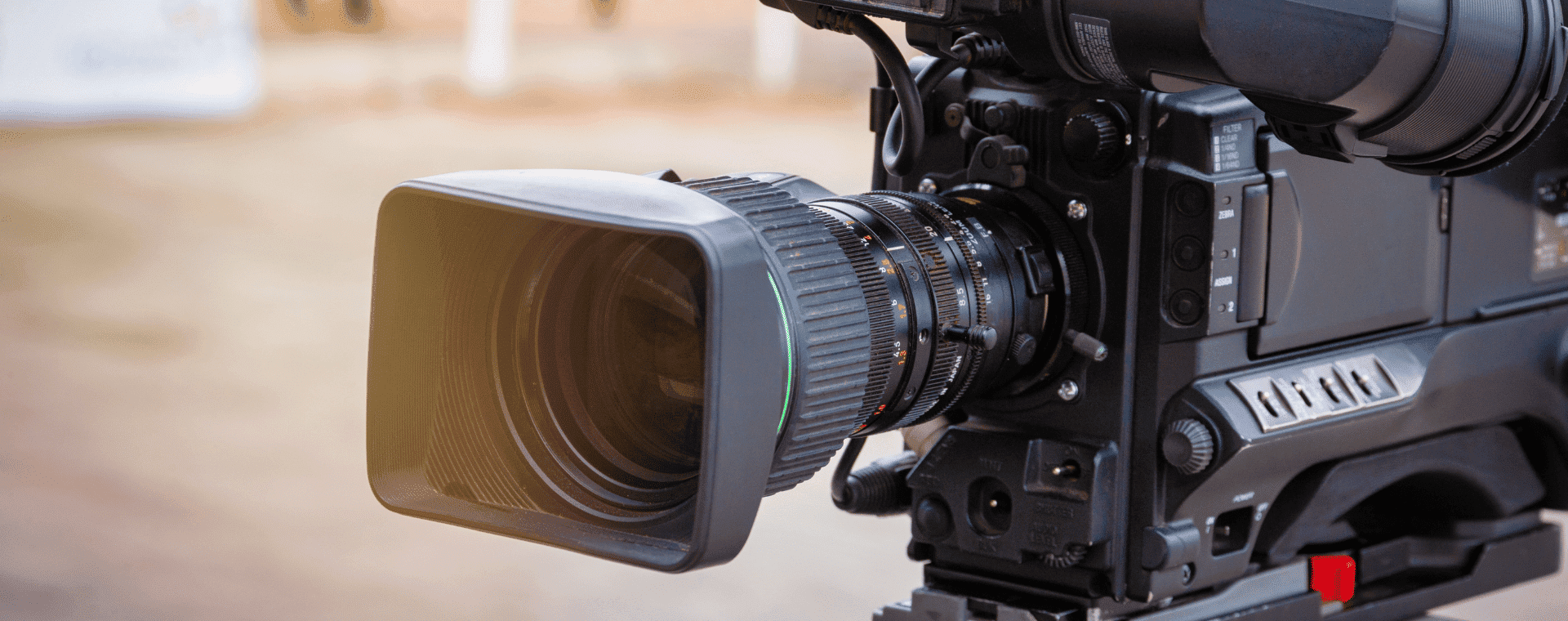 Close-up of a 4k professional camera with a large lens and various control knobs and buttons on its side. Positioned outdoors with a blurred background, this setup suggests the camera is ready for filming on location.