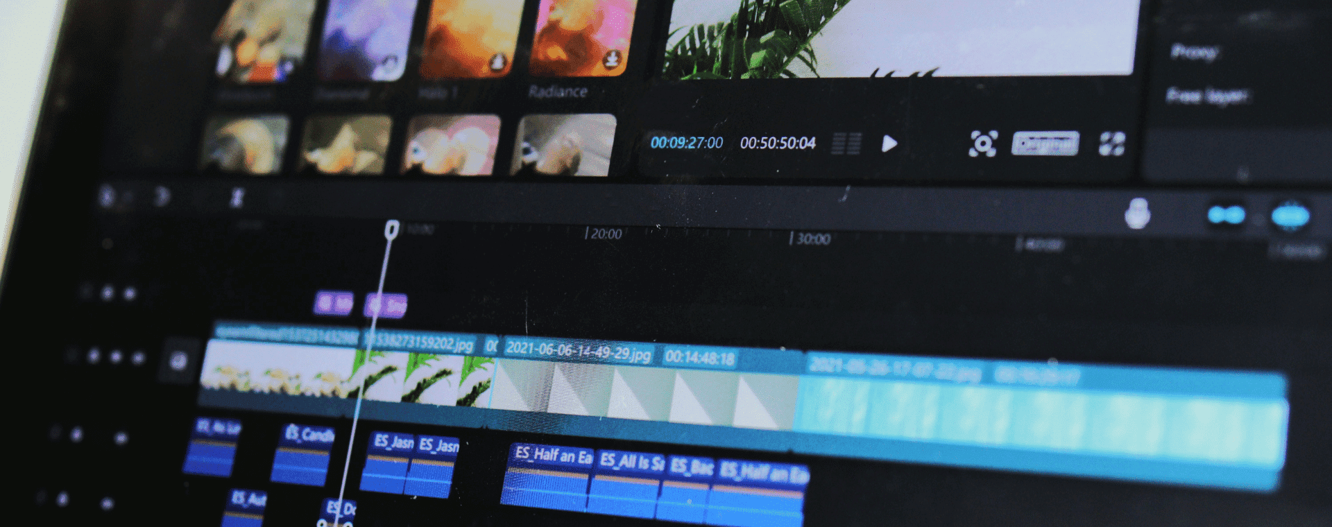Close-up of a video editing timeline on a computer screen. Various video clips, audio tracks, and effects are visible, with some displaying thumbnails and others marked by colored bars and time codes. Captured with 4k professional cameras, the interface has multiple editing tools and a dark theme.