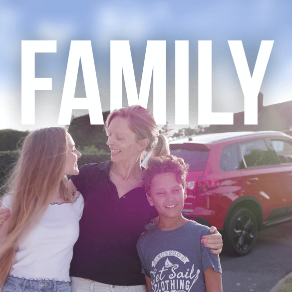 A mother stands smiling with her two children, an older daughter and a younger son, in front of a red SUV on a sunny day. They appear happy and affectionate, holding each other closely. The word "FAMILY" is boldly displayed above them—a picture-perfect moment captured through professional video production services.