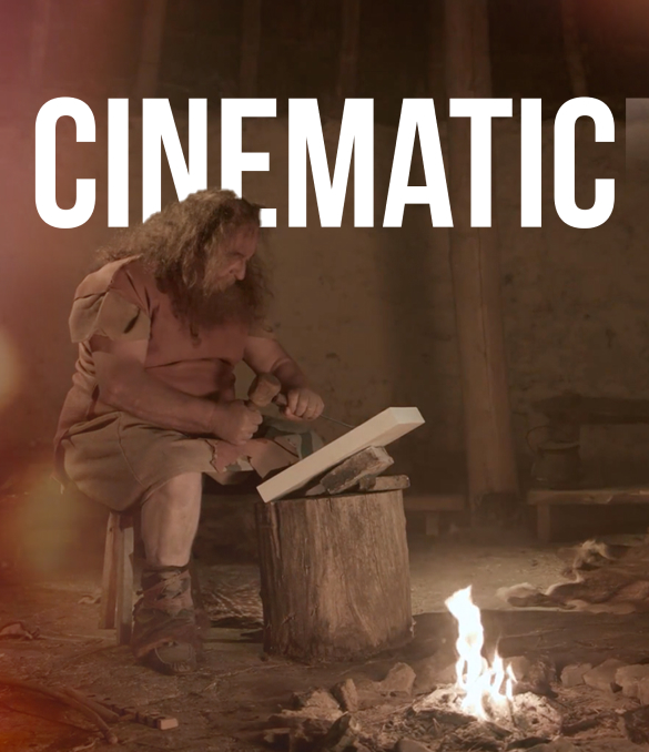 A person with long hair and a beard, wearing brown rustic attire, sits on a wooden stool carving a piece of wood with a knife. There is a small fire burning on the ground nearby. "CINEMATIC" is boldly displayed at the top of the image, showcasing our video production services in action.