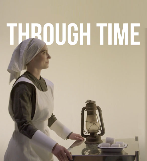 A person dressed in historical clothing, including a white bonnet and apron, stands next to an old-fashioned oil lamp and soap bars on a metal table. The text "THROUGH TIME" is displayed prominently at the top of the image, reminiscent of an NHS promotional video celebrating healthcare history.