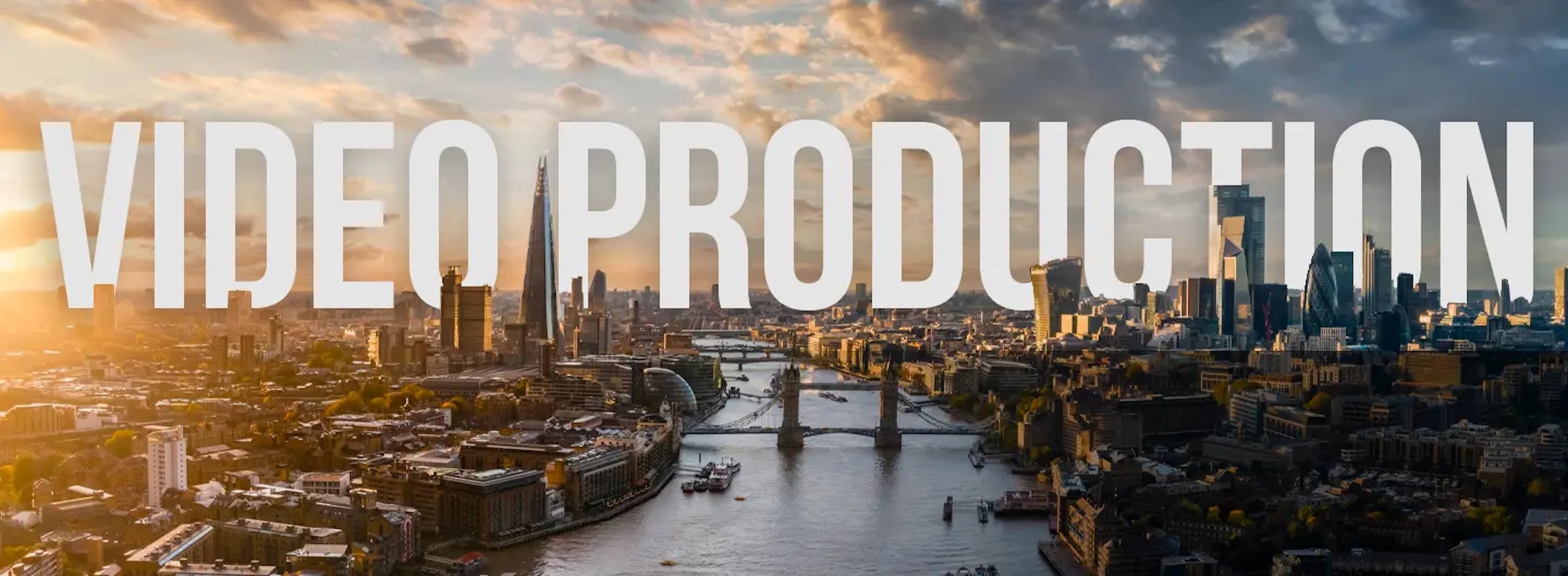 Aerial view of a cityscape at sunset, showcasing iconic architectural landmarks and a river flowing through the center. The sky is partly cloudy with a golden hue from the setting sun. Large white text overlay reads "VIDEO PRODUCTION" – perfect for enhancing your video portfolio.