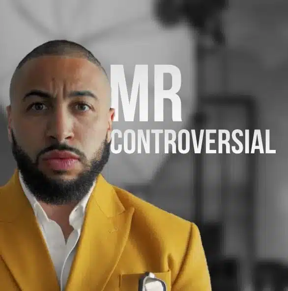 A man with a beard wearing a mustard yellow jacket stands with a serious expression. The background is in black and white, blurred, with the text "MR CONTROVERSIAL" in bold white letters next to him, as if he's starring in an intense promotional video.