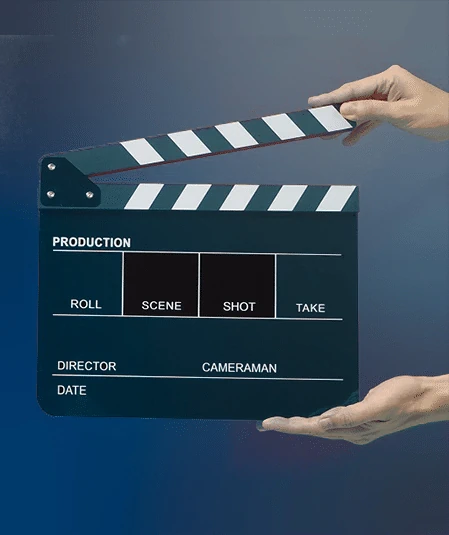 Hands holding a movie clapperboard against a blue background. The clapperboard, an essential video production resource, has spaces for "Production," "Roll," "Scene," "Shot," "Take," "Director," "Cameraman," and "Date." The top part is being raised, indicating the start of filming.
