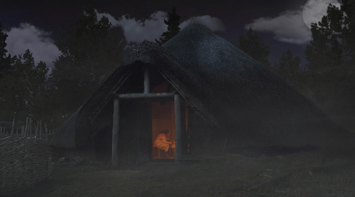 A thatched-roof hut is illuminated from within, revealing a person seated inside, bathed in warm light. The hut is surrounded by trees under a night sky with a bright moon partially obscured by clouds. A woven fence is visible on the left side of the image, capturing a scene perfect for video production services.
