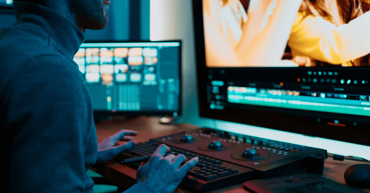 A video editor is working at an editing station with multiple monitors. One screen displays a sequence of video clips, while another shows a video editing timeline. The desk is equipped with professional editing tools and consoles, all illuminated by cool lighting.