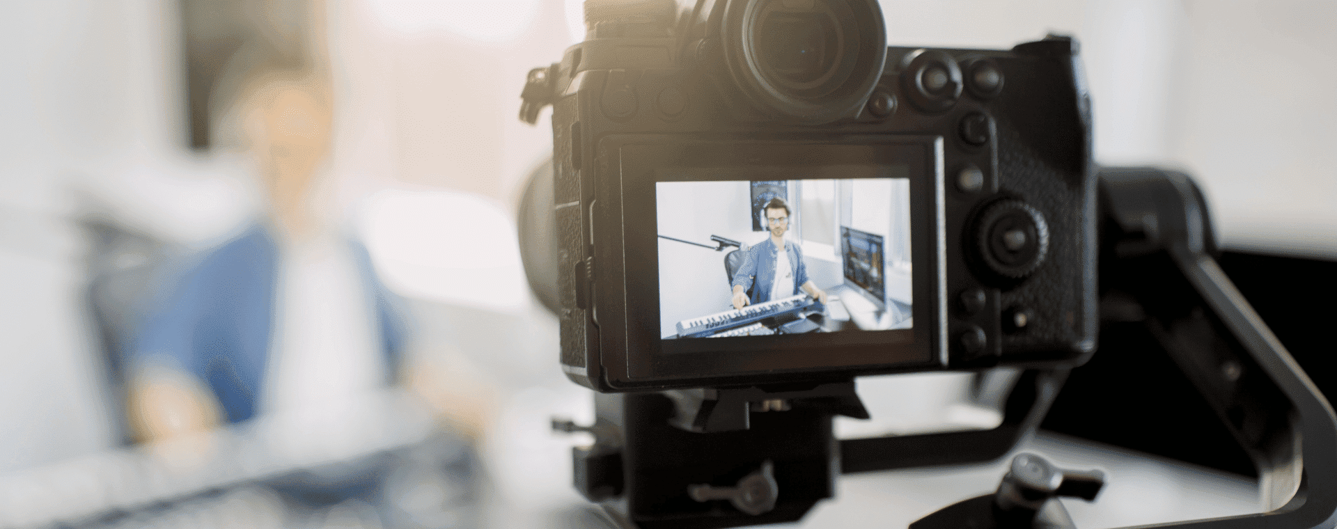 Close-up of a camera screen displaying a person playing a keyboard musical instrument. The person is seated in a blurred background, suggesting the photo is being taken during a live recording or streaming session, potentially for b2b marketing purposes.