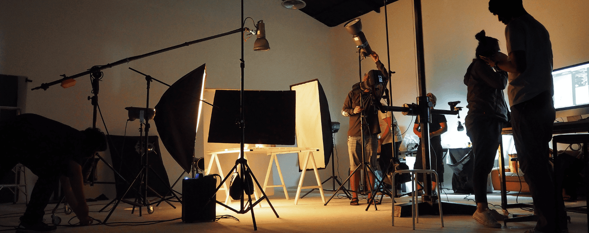 A studio setup with various pieces of photography equipment, including tripods, lights, and reflective screens is bustling with activity as several people adjust the gear in preparation for a photoshoot, creating a busy and dynamic environment perfect for b2b marketing materials.