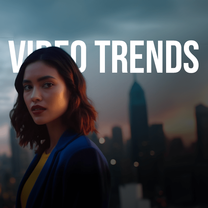A woman with shoulder-length dark hair, wearing a blue jacket over a yellow top, stands in front of an urban skyline at dusk. The text "VIDEO TRENDS" is prominently displayed in bold white letters above her head.
